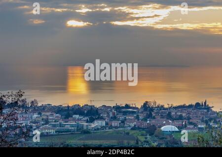 Blick auf Bardolino von den Hügeln. Auf diesen Hügeln befinden sich die Weinberge des berühmten Bardolino-Weins. Der Sonnenuntergang spiegelt sich im Gardasee wider. Stockfoto