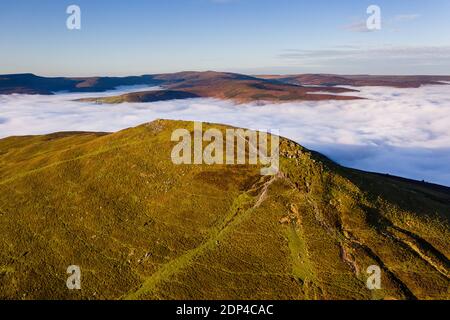 Luftaufnahme eines Berggipfels, der über einem Meer niedriger Wolken und Nebel im Tal darunter aufsteigt (Sugar Loaf, Brecon Beacons, Wales) Stockfoto