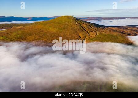 Luftaufnahme eines Berggipfels, der über einem Meer niedriger Wolken und Nebel im Tal darunter aufsteigt (Sugar Loaf, Brecon Beacons, Wales) Stockfoto