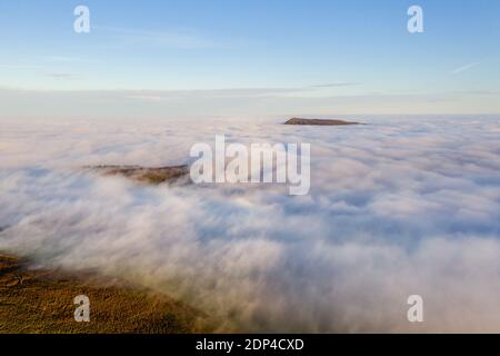 Luftaufnahme der Berge, die an einem hellen, sonnigen Tag über einem Nebelmeer aufsteigen. Stockfoto