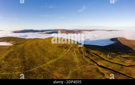 Panorama-Luftaufnahme eines Berggipfels, der über einem Meer aus niedriger Wolke und Nebel aufsteigt (Sugar Loaf, Wales). Stockfoto