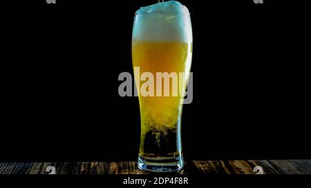 Helles Bier in einem Bierglas auf schwarzem Hintergrund in Nahaufnahme, frisches Bier in ein Glas gießen. Stockfoto