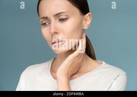 Nahaufnahme der kranken traurigen Frau, die Lymphknoten überprüft, erkältet, an Kehlkopfproblemen leidet, isoliert auf blauem Hintergrund im Studio Stockfoto