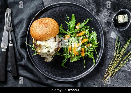 Leckere Burger mit Blauschimmelkäse, Speck, marmorierte Rind- und Zwiebelmarmelade, eine Beilage mit Salat mit Rucola und Orangen. Schwarzer Hintergrund. Draufsicht Stockfoto