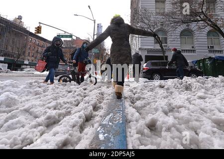 Nach dem ersten Schneesturm der Saison während der COVID-19 Pandemie versucht eine Frau, ihr Gleichgewicht zu halten, wenn sie über ein Holzbrett geht, das über einer Straßenecke auf Manhattans Upper West Side, New York, NY, am 18. Dezember 2020 pfützt. Aufgrund der steigenden Rate von Coronavirus-Infektionen in der Stadt und einem Anstieg in den Vereinigten Staaten, New York City hat eine weitere Runde von Beschränkungen für Indoor-Restaurants auferlegt; Die Nor'easter brachte mehr als einen Fuß Schnee in einem Teil von New York City, einem linken Teil von Upstate New York mit etwa 40 Zoll Schnee bedeckt, so dass Straßen glatt und gefährlich für dri Stockfoto