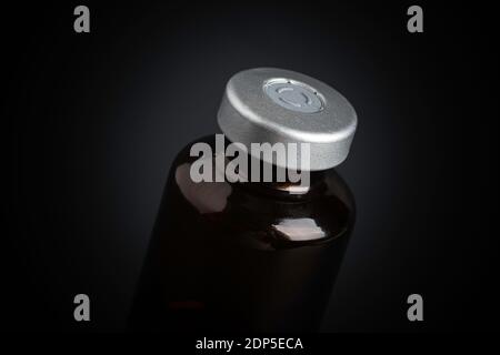 Eine Makroaufnahme mit selektivem Fokus auf einer bernsteinfarbenen Impfstoffflasche auf einem dramatischen schwarzen Hintergrund. Stockfoto