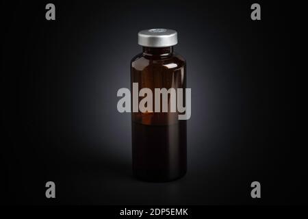 Eine Makroaufnahme mit selektivem Fokus auf einer bernsteinfarbenen Impfstoffflasche auf einem dramatischen schwarzen Hintergrund. Stockfoto