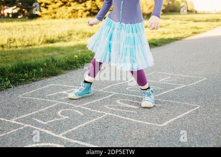 Nahaufnahme von Kind Mädchen spielen springen hopscotch im Freien. Lustige Aktivität Spiel für Kinder auf dem Spielplatz draußen. Sommer Hinterhof Street Sport für Kinder Stockfoto