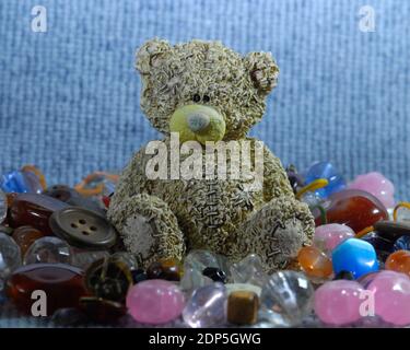Nahaufnahme einer braunen Bärenfigur sitzend und umgeben von bunten Perlen und Knöpfen mit weichem Hintergrund. Stockfoto