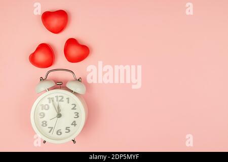 Rosa Hintergrund mit weißem Wecker und roten Herzen. Kreatives Layout. Draufsicht. Zeit für Liebe und Grüße Stockfoto