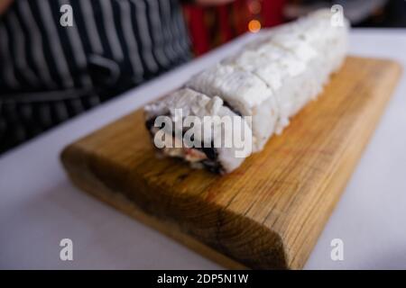 Sushi-Brötchen mit weißer Creme auf Schneidebrett bedeckt Stockfoto