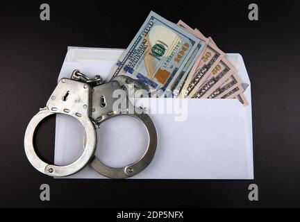 Handschellen auf dem Umschlag mit einem American Dollars auf dem Schwarzer Papierhintergrund Stockfoto