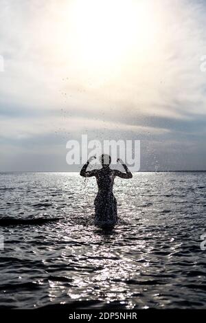 Man Silhouette mit Spritzern im Wasser bei Sonnenuntergang Hintergrund Stockfoto