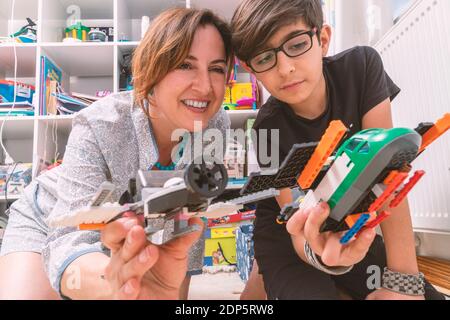 Kaukasische junge Frau spielt mit ihrem Sohn. Sie lassen kleine Flugzeuge fliegen. Sie sitzen auf dem Boden im Kinderzimmer und genießen Stockfoto