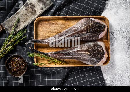 Frischer Seeteufel ohne Kopf auf einem Holztablett mit einem Spalter. Grauer Hintergrund. Draufsicht. Stockfoto