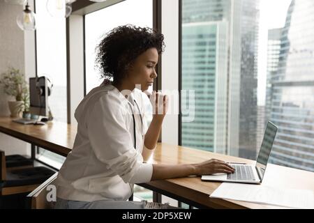 Pensive biracial Frau arbeiten auf Laptop im Büro Stockfoto