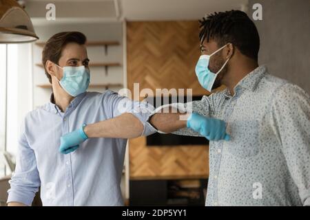 Multirassische Männchen in Masken berühren Ellbogen Gruß während covid-19 Stockfoto