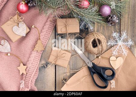 Geschenkverpackung Weihnachtsgeschenke in Bastelpapier. Das Konzept der Vorbereitung auf Weihnachten und das neue Jahr. Basteln Sie Papier, Scheren, Geschenke, Christbaumzweige und Schneeflocken. Draufsicht Stockfoto