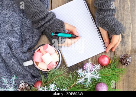 Neujahrsvorsätze mit Weihnachtsschmuck. Tasse mit einem heißen Getränk mit Marshmallows auf dem Holztisch. Draufsicht. Stockfoto