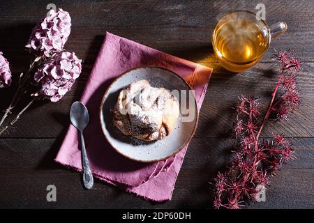 Tea Time - dampfender Tee mit einem Nuss-Cookie bestreut Mit Puderzucker auf einem braunen Holztisch verziert mit Blumen Stockfoto