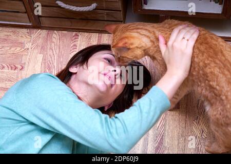 Schöne Frau mit Blick auf ihre orange Katze liegt auf dem Boden zu Hause. Konzept Liebe für Tiere Stockfoto