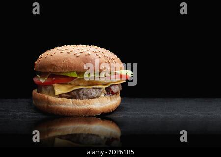 Burger, Cheeseburger, mit Fleischschnitzel, Käse, Salat und Tomaten, auf schwarzem Hintergrund, mit Reflexion und Platz für Text Stockfoto