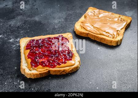 Erdnussbutter und Gelee auf Weißbrot Toasts. Schwarzer Hintergrund. Draufsicht. Stockfoto