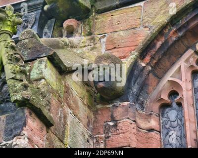 Ein altes Gesicht und Kopf in Sandstein geschnitzt auf der Außenseite der St. Oswald's Parish Church in Malpas, Cheshire, Großbritannien. Stockfoto