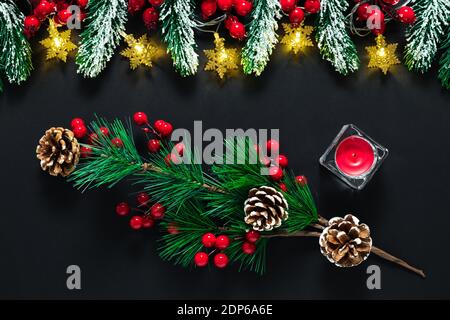 Schwarze Weihnachtskarte, Neujahrshintergrund mit grünen Tannenzweigen, Tannenzapfen, roten Beeren und Kerze. Winterurlaub Konzept, Ornament pa Stockfoto