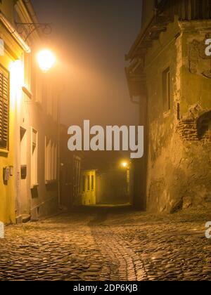 Nachtszene aus der Zitadelle von Sighisoara mit Kopfsteinpflasterstraßen, alten mittelalterlichen Gebäuden und einem Laternenpfosten Stockfoto