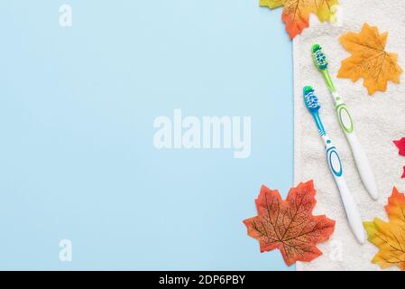 Zwei Zahnbürsten auf weißem Handtuch mit Herbstblättern auf blau Hintergrund mit Kopierbereich Stockfoto