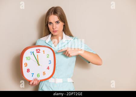 Portrait der verärgerten Krankenschwester, die auf die Uhr zeigt. Stockfoto