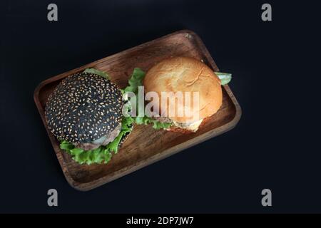 Zwei Hamburger auf Holzplatte isoliert auf schwarzem Hintergrund flach legen. Das Bild enthält den Kopierbereich Stockfoto