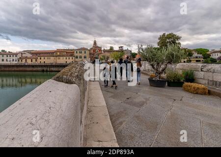 Die Menschen gehen auf der alten Tiberius-Brücke im historischen Zentrum von Rimini, Italien, unter einem dramatischen Himmel Stockfoto