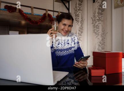 Glückliche asiatische Frau trägt blauen Pullover mit einem Glas Champagner, im Gespräch mit der Familie, soziale Distanz Freund von Videokonferenz Gespräch Gespräch ein Stockfoto