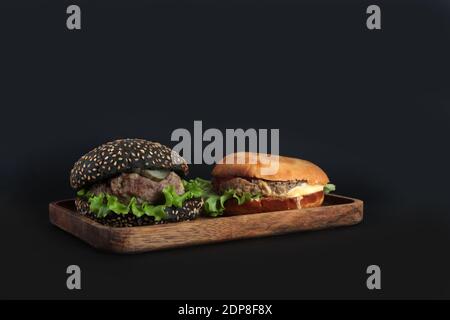 Zwei Hamburger auf Holzplatte isoliert auf schwarzem Hintergrund. Das Bild enthält den Kopierbereich Stockfoto