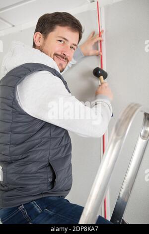 Glücklicher junger Mann hämmerte Nagel in die Wand Stockfoto