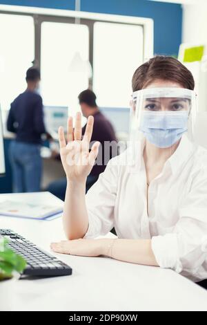 Unternehmer, der virtuelle Konferenz mit Geschäftsreisenden aus dem Büro des Unternehmens trägt Gesichtsmaske. Pov des Managers, der während eines Online-Anrufs mit einem Remote-Team spricht, während Kollegen im Hintergrund arbeiten. Stockfoto