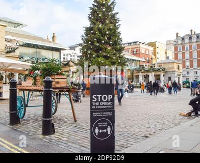 Die Menschen gehen an einem Schild "Stoppen Sie die Ausbreitung des Coronavirus" und dem Weihnachtsbaum auf dem Covent Garden Market vorbei. London wird noch strengere Beschränkungen auferlegen, da die Fälle ansteigen und in der Hauptstadt und im Südosten Englands eine neue Sorte COVID-19 entsteht. Stockfoto