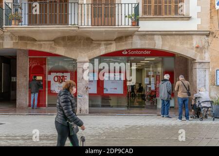 Llucmajor, Spanien; dezember 17 2020: Fassade einer spanischen Bank mit Kunden, die eine Gesichtsmaske tragen und aufgrund der von Coronaviru ergriffenen Maßnahmen draußen warten Stockfoto