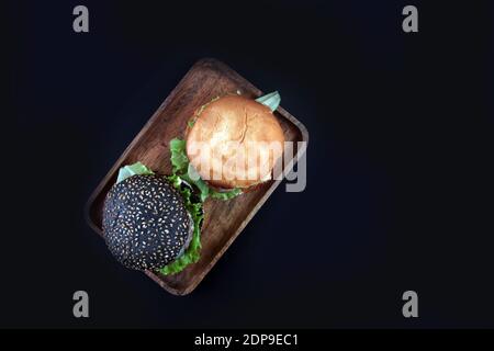 Zwei Hamburger auf Holzplatte isoliert auf schwarzem Hintergrund flach legen. Das Bild enthält den Kopierbereich Stockfoto