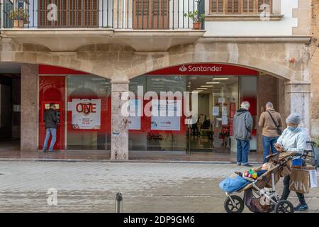 Llucmajor, Spanien; dezember 17 2020: Fassade einer spanischen Bank mit Kunden, die eine Gesichtsmaske tragen und aufgrund der von Coronaviru ergriffenen Maßnahmen draußen warten Stockfoto