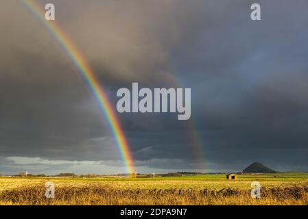 East Lothian, Schottland, Großbritannien, 19. Dezember 2020. UK Wetter: Ein auffälliger doppelter Regenbogen erscheint nach Regen und schaut in Richtung Berwick Law über Felder bei Sonnenschein Stockfoto