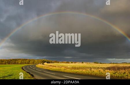 East Lothian, Schottland, Großbritannien, 19. Dezember 2020. UK Wetter: Ein auffälliger Regenbogenbogen erscheint nach Regen, der sich über eine Landstraße bei Sonnenschein wölbt Stockfoto