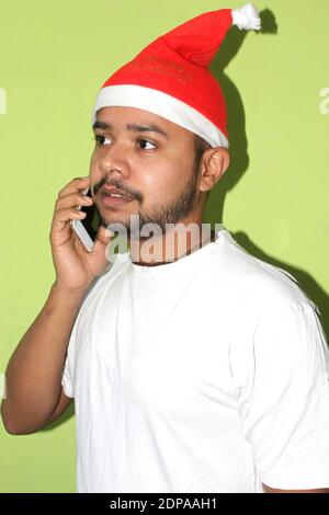 Mann mit weihnachtshut telefoniert, Weihnachtsfeier auf grünem Hintergrund, selektiver Fokus mit Unschärfe. Stockfoto