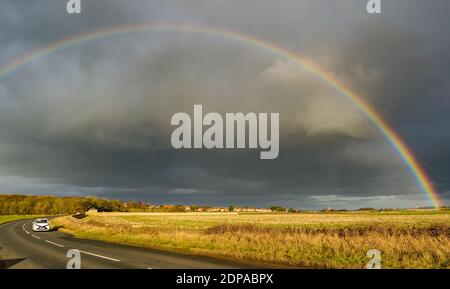 East Lothian, Schottland, Großbritannien, 19. Dezember 2020. UK Wetter: Ein auffälliger Regenbogenbogen erscheint nach Regen, der sich über eine Landstraße bei Sonnenschein wölbt Stockfoto