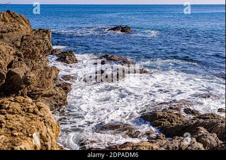 Mittelmeerküste im Süden Frankreichs. Die roten Felsen des Esterel steigen ins Meer ab. Wellen brechen auf den Felsen verursachen einen weißen Schaum. Stockfoto