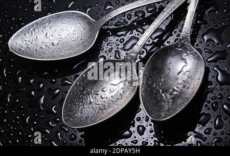 Drei Stahllöffel mit Wassertropfen auf schwarzem Hintergrund Stockfoto