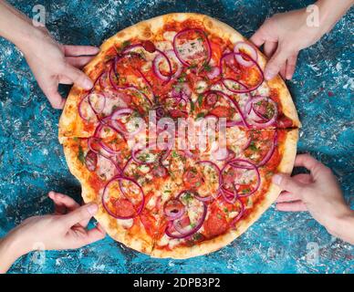 Hand nimmt ein Stück hausgemachte Pizza auf einem blauen Beton background.Company Freunde. Freundlicher Snack. Draufsicht Stockfoto