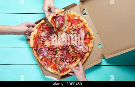 Hand nimmt ein Stück Pizza auf einen blauen Tisch. Unternehmensfreunde. Freundlicher Snack. Draufsicht. Stockfoto